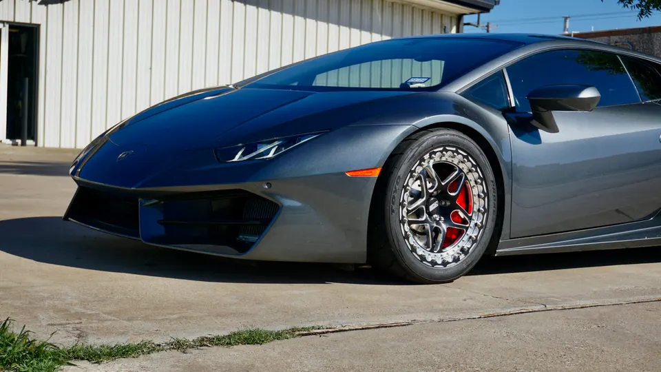 A grey Lamborghini Huracan with aftermarket multi-piece wheels and red brake calipers parked outdoors.