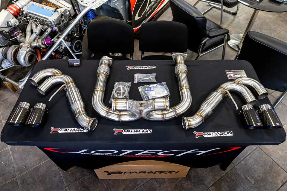 Paragon Performance stainless steel exhaust system with carbon fiber tips displayed on a Jotech Motorsports table.