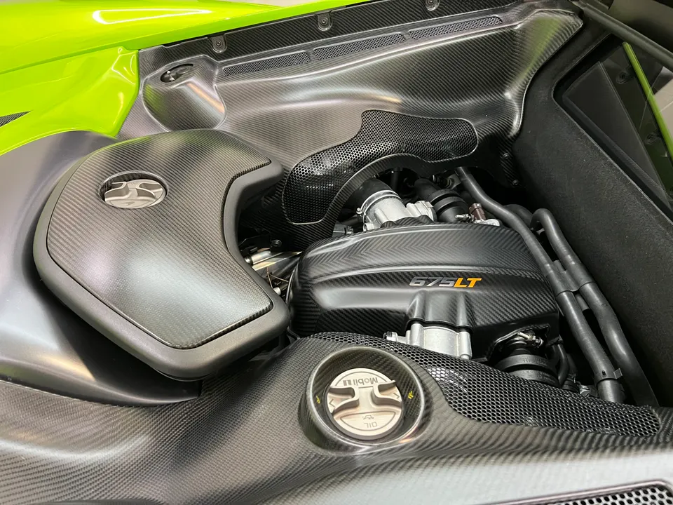 Close-up of a McLaren 675LT engine bay with carbon fiber components and a vibrant green body panel.