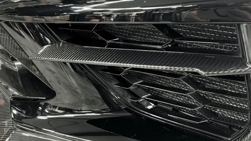 A close-up of a car's front grille featuring carbon fiber accents and a honeycomb mesh design.