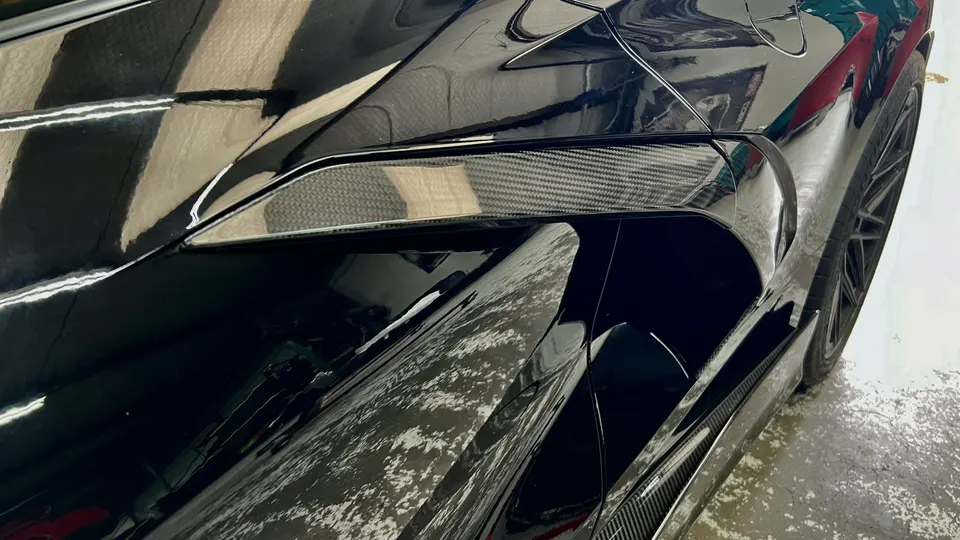 Close-up of a black supercar's rear quarter panel with carbon fiber aerodynamic trim.