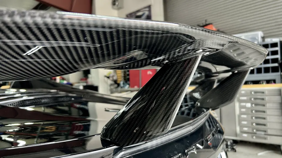 Close-up of a carbon fiber rear wing on a performance car, showcasing the weave and aerodynamic design.