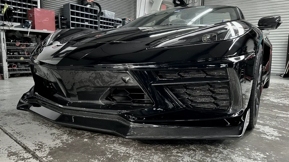 A black C8 Corvette with a carbon fiber front splitter and aero kit in a performance tuning shop.
