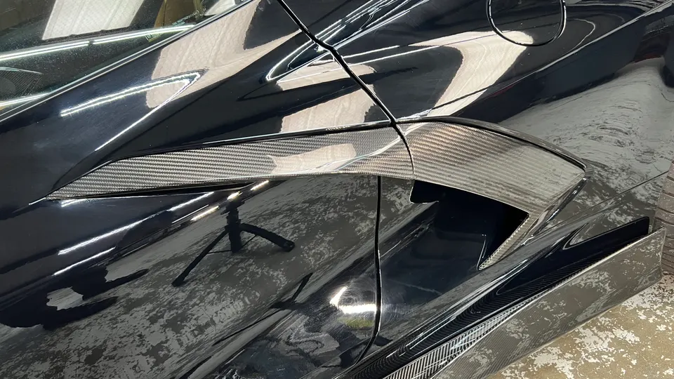 Close-up of a black C8 Corvette's side with a carbon fiber air intake vent and glossy paint finish.