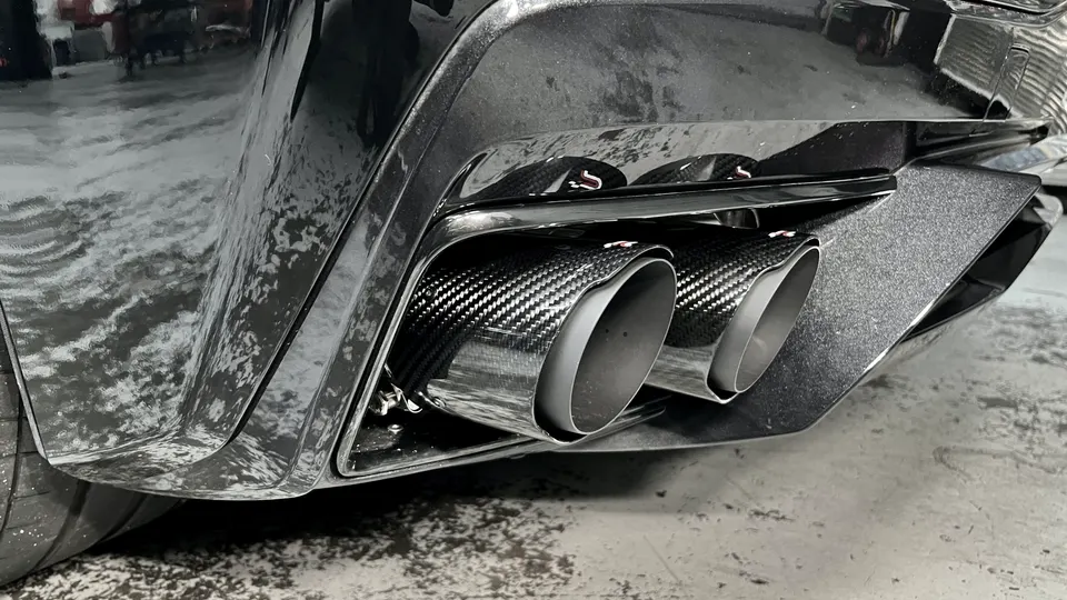 Close-up of a black car's quad carbon fiber exhaust tips and rear diffuser, showcasing aftermarket performance parts.