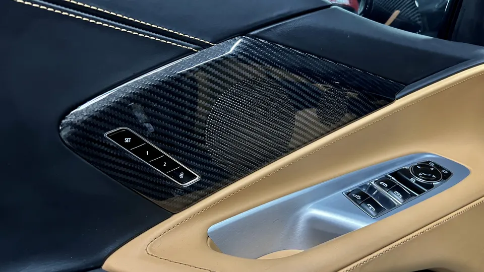 Close-up of a car's interior door panel featuring carbon fiber trim, speaker, memory seat buttons, and window controls.