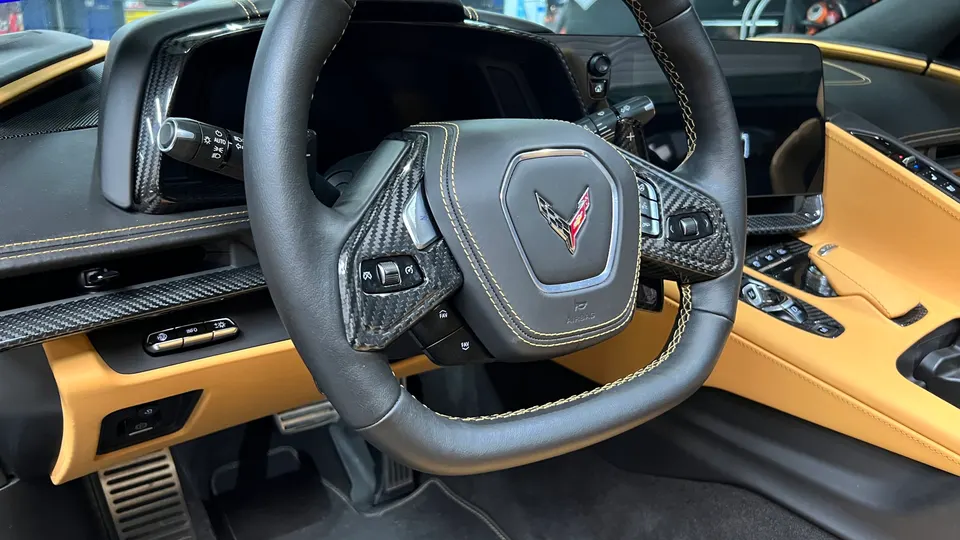 Detailed view of the Chevrolet Corvette C8 interior, showcasing the carbon fiber steering wheel and tan leather trim.