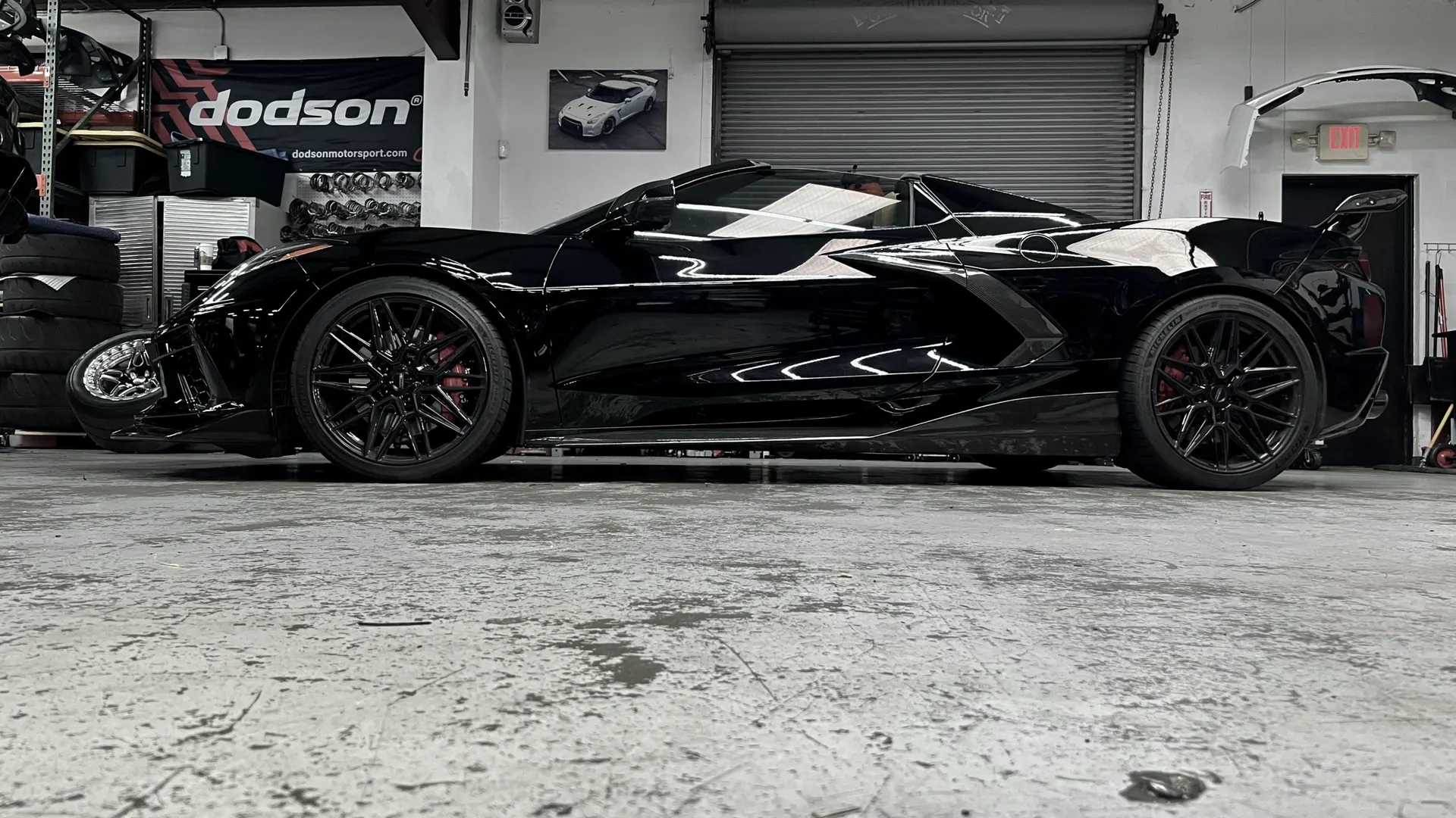 Black C8 Corvette with aftermarket wheels parked in a performance tuning shop.
