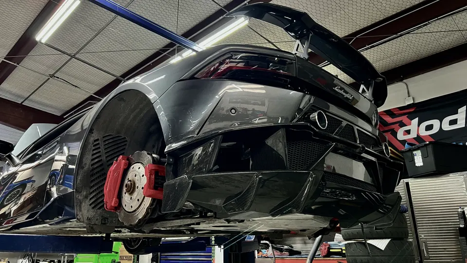 Lamborghini Huracan on a lift in a performance shop, showcasing its carbon fiber rear diffuser, large wing, and red brake calipers.