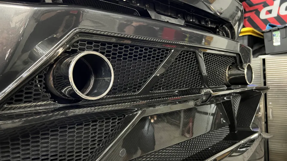 Close-up of a car's rear bumper featuring carbon fiber diffuser, honeycomb grilles, and polished exhaust tips.