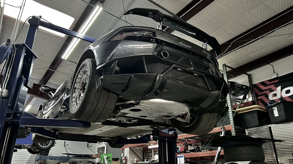 A black Lamborghini Huracan on a lift in a performance shop, showcasing its carbon fiber rear diffuser and large wing.