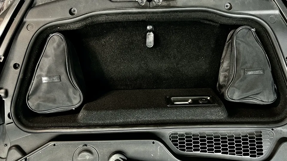 A detailed view of a McLaren's frunk, showing the carpeted storage area and two triangular luggage bags.