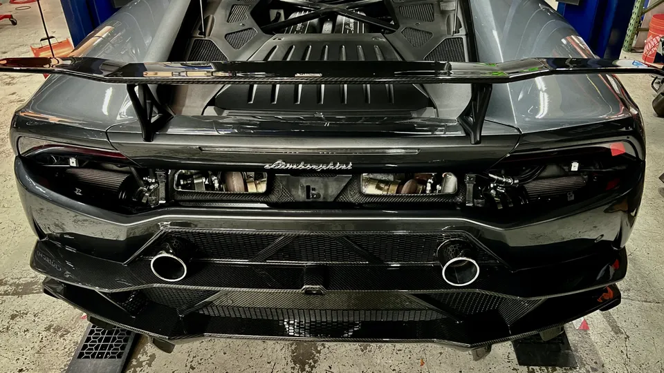 Rear view of a grey Lamborghini Huracan in a shop, featuring a large carbon fiber wing and aftermarket exhaust.
