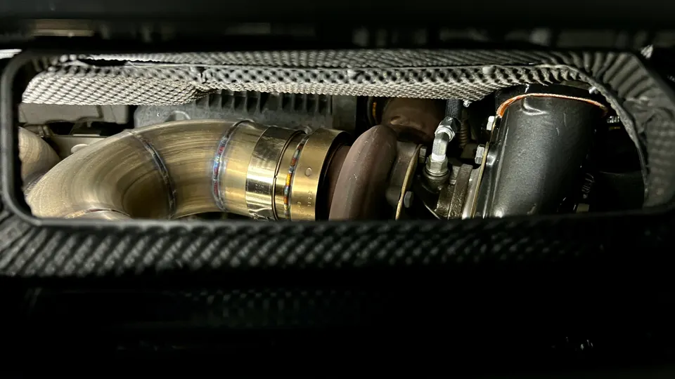 Close-up view of a custom turbocharger and downpipe with heat shielding in a high-performance vehicle's engine bay.