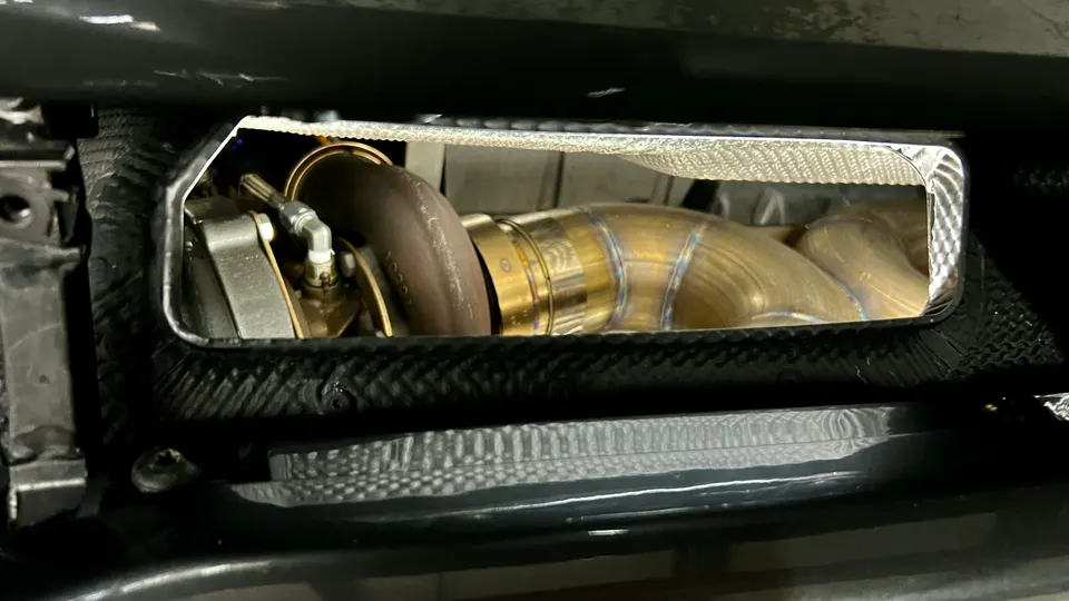 Close-up of a performance turbocharger and exhaust piping with heat shielding visible in a car's engine bay.