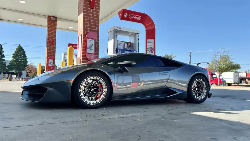 A grey Lamborghini Huracan with custom aftermarket wheels parked at a Mobil gas station on a sunny day.