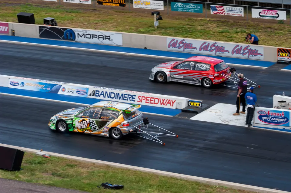 Two highly modified Honda Civic drag cars with wheelie bars on the track at Bandimere Speedway, preparing for a race