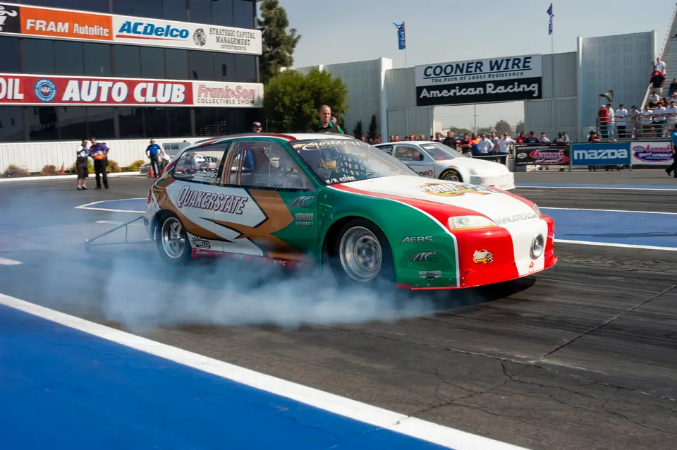 A race-prepped Honda Civic hatchback performs a burnout at a drag strip, with smoke billowing from its tires.