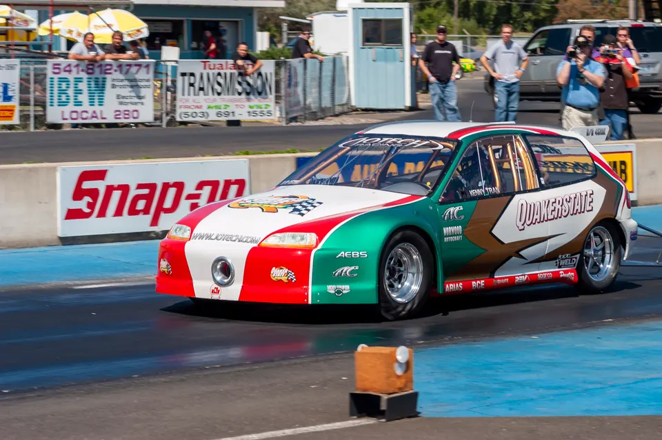 A red, white, and green Honda Civic drag race car on a track with "Quakerstate" and "Jotech" branding.