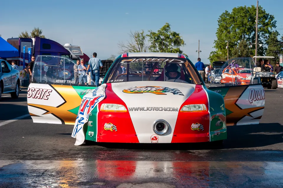A red, white, and green Jotech drag race car with 'Kenny Tran' on the side, parked at a track.