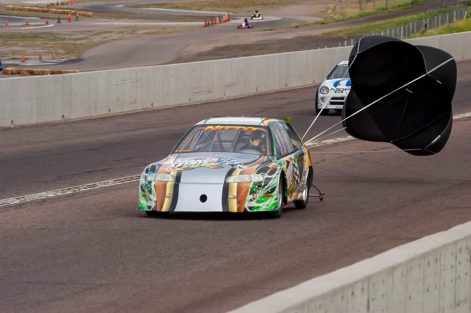 A custom-built drag racing Honda Civic deploying its parachute on a track after a run, with another car in the background.
