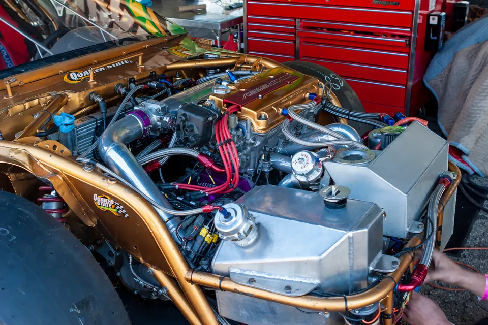 Highly modified gold engine bay of a drag racing car with a Turbonetics wastegate and custom boost piping in a shop.