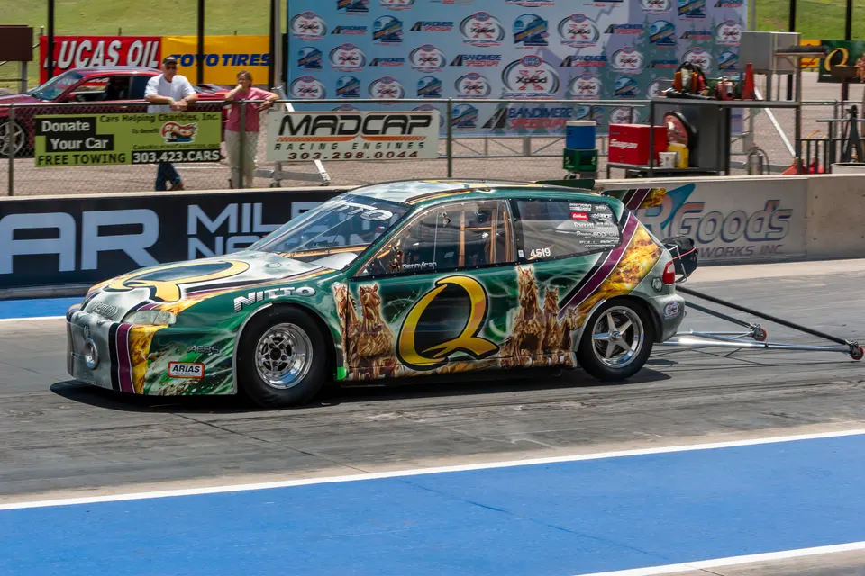 A custom-wrapped green and gold Honda Civic drag car with wheelie bars on a drag strip.