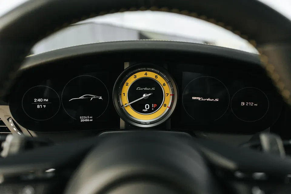 A close-up view of a Porsche 911 Turbo S digital instrument cluster showing the speedometer, tachometer, and other displays.