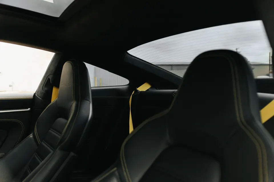 Interior view of a Porsche with black leather seats and yellow seatbelts, showcasing the cabin details.