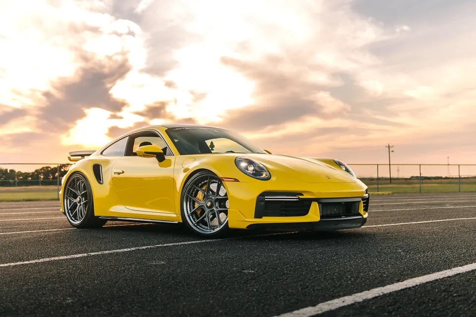 Yellow Porsche 911 (992 Turbo S) with aftermarket wheels parked on a track at sunset, showcasing its sleek design.