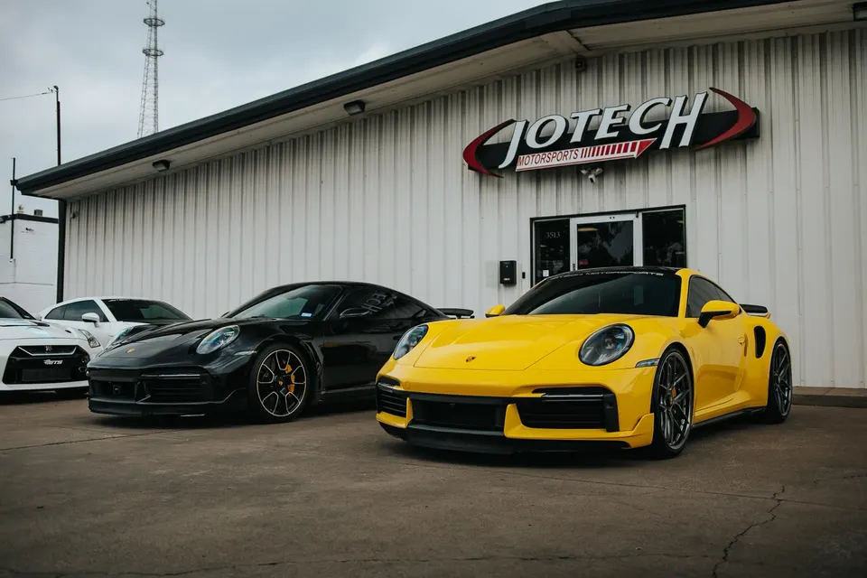 Yellow and black Porsche 911s and a white Nissan GT-R parked outside Jotech Motorsports performance tuning shop.