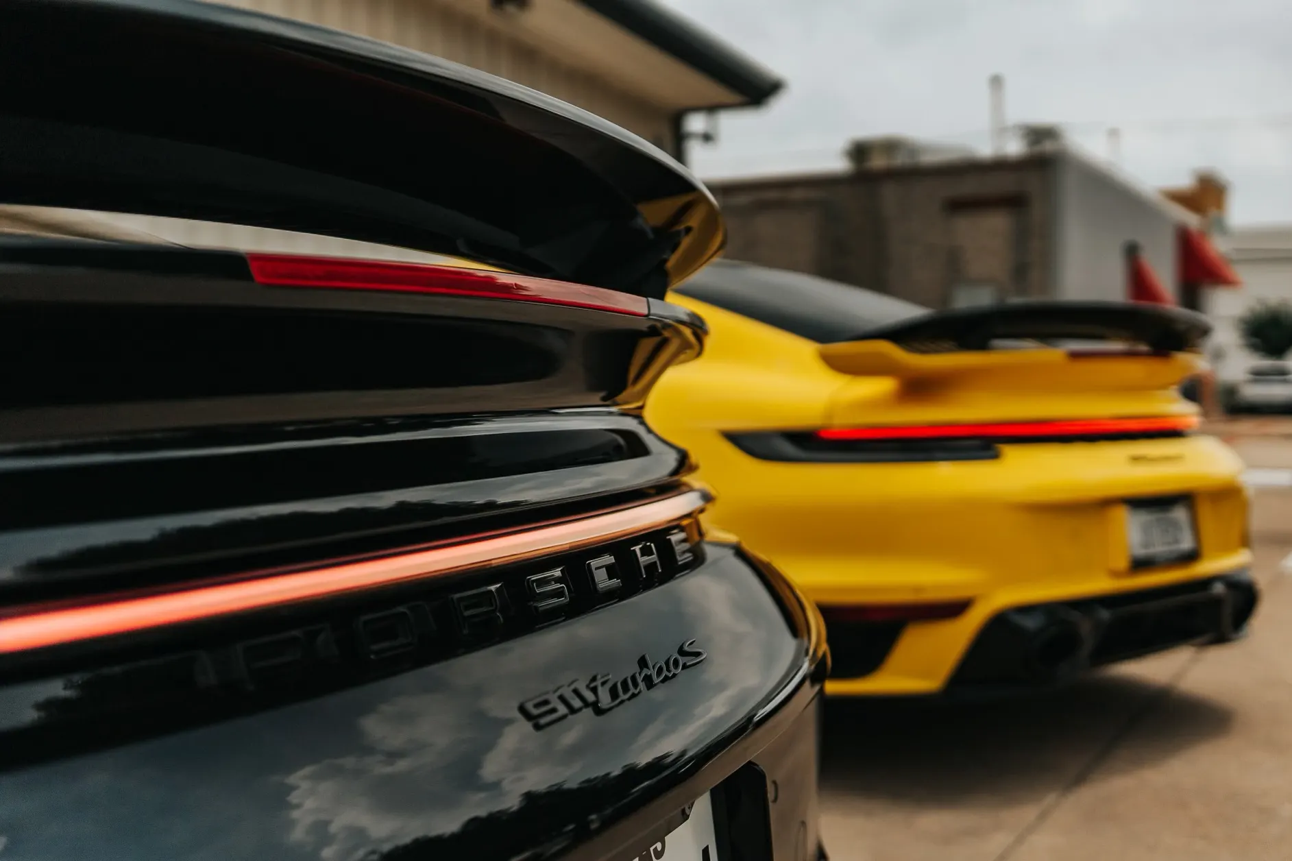 Two Porsche 911 Turbo S cars, one black and one yellow, parked with a focus on their rear badging and taillights.