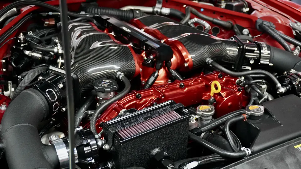 Close-up of a custom high-performance engine bay with carbon fiber intake manifolds, red engine components, and upgraded fuel system.
