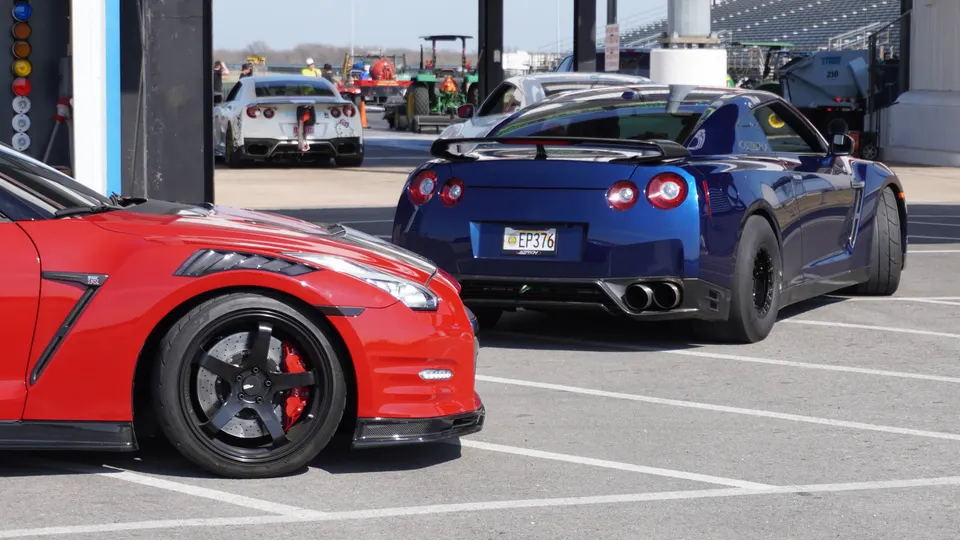 Multiple modified Nissan GT-R R35s, including a red and a blue one, parked at a drag strip staging area.