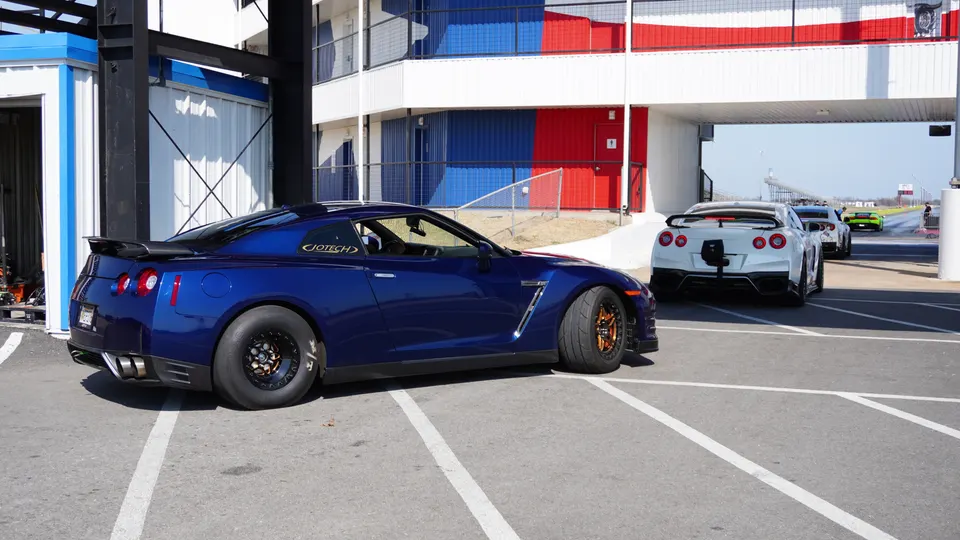 Blue Nissan GT-R with drag slicks in the foreground at a race track, with other GT-Rs in the staging lane.