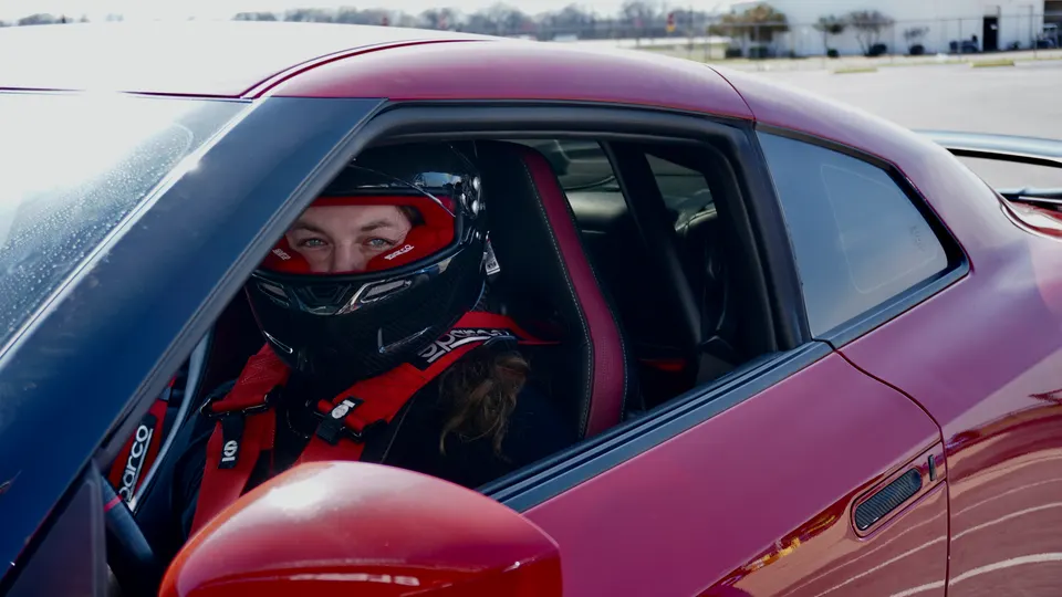 Driver wearing a racing helmet and Sparco harness in the interior of a red Nissan GT-R at a track event.