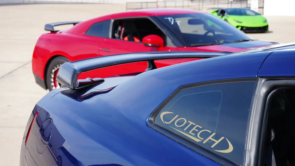 Blue and red Nissan GT-Rs with a green Lamborghini at a track event, featuring a Jotech decal on the blue GT-R.