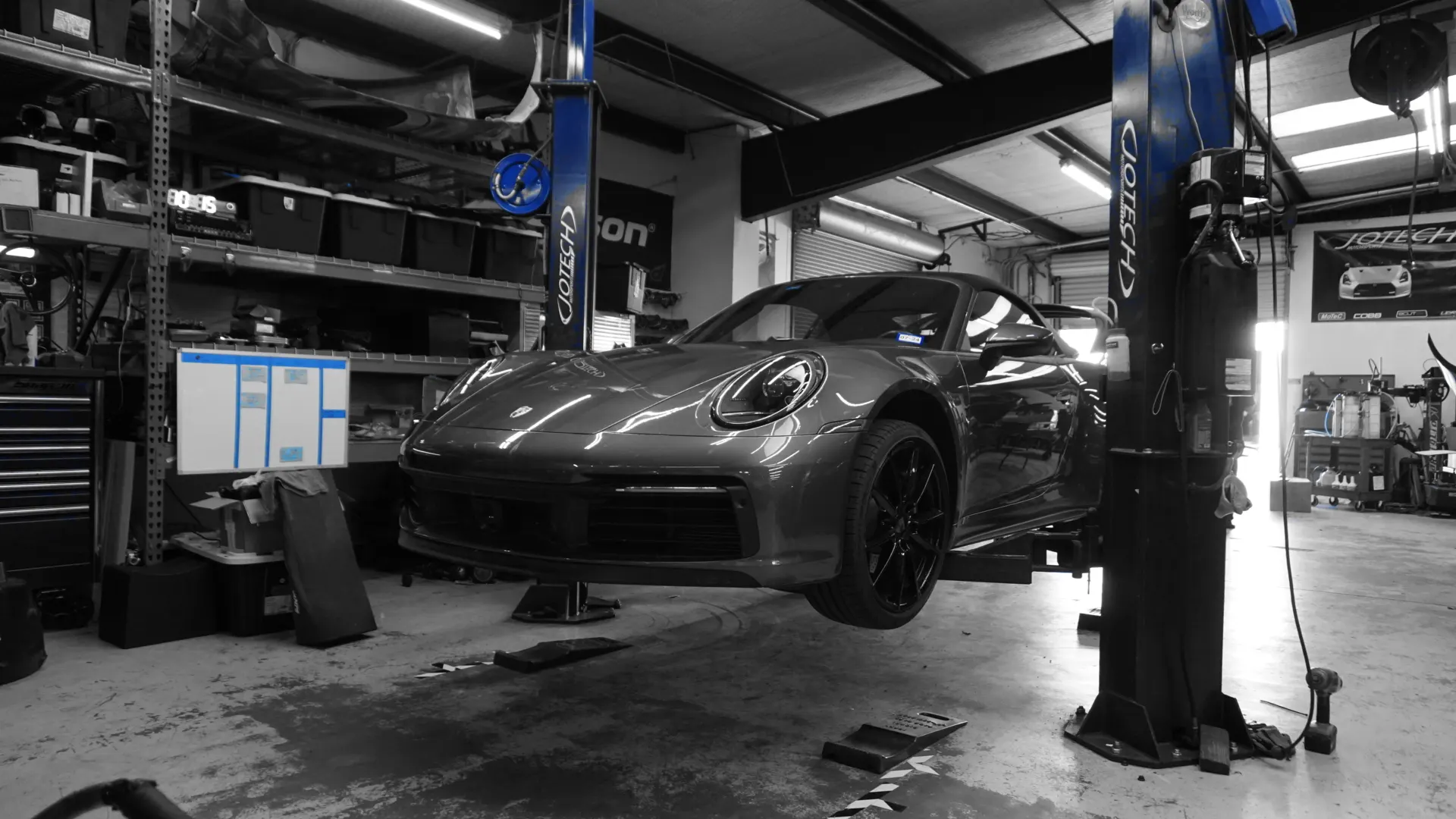 A grey Porsche 911 on a blue hydraulic lift inside the Jotech Motorsports performance tuning shop.