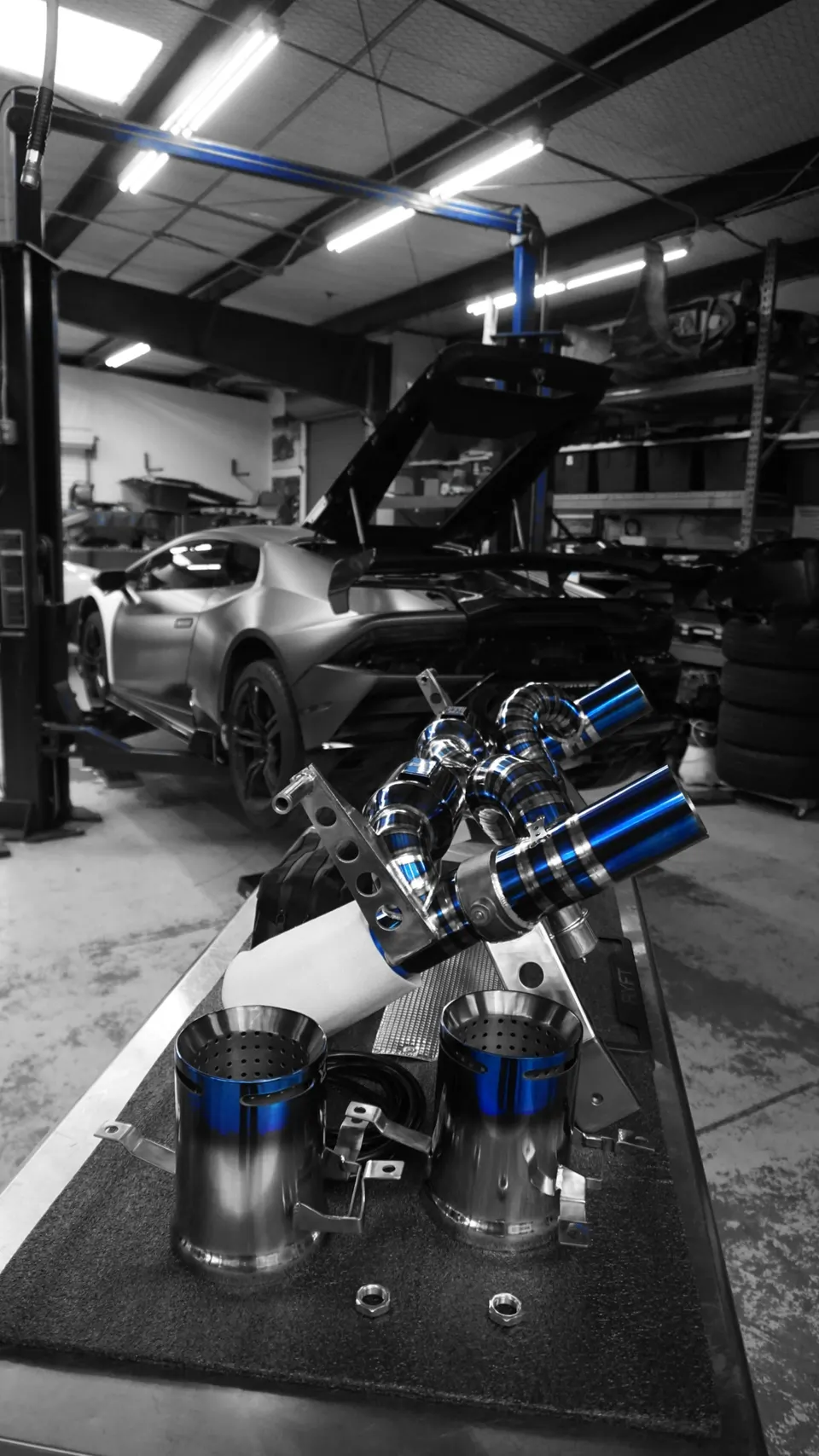 Lamborghini Huracan on a lift in a performance shop with a titanium exhaust system laid out on a workbench.