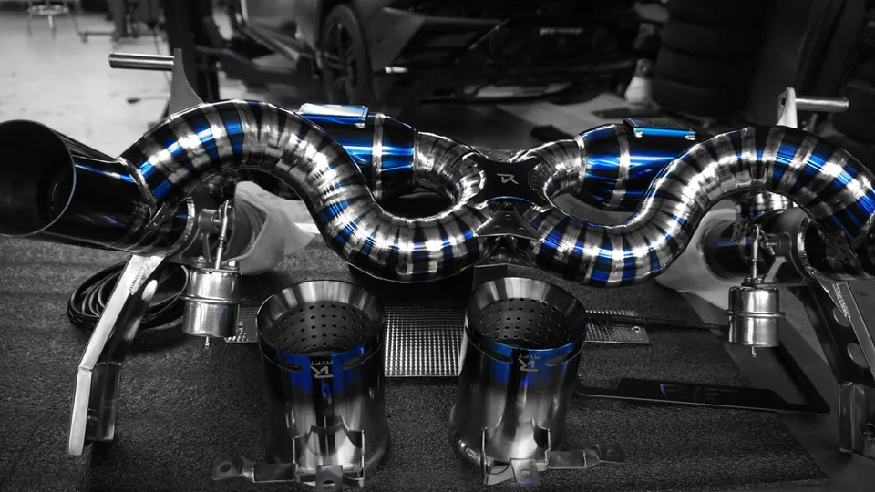 Aftermarket titanium exhaust system with blue accents and tips laid out in a performance shop.