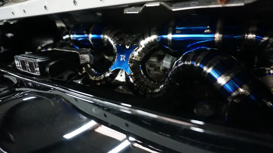 Close-up of a custom titanium exhaust system with blue accents and intricate piping in an engine bay.