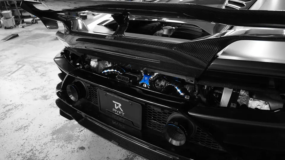 Rear view of a black Lamborghini with exposed engine bay showcasing blue aftermarket turbo/boost piping and carbon fiber aero parts in a tuning shop.