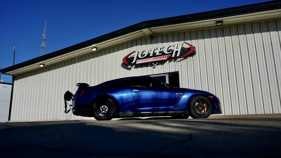 Blue Nissan GT-R with drag setup and parachute parked outside Jotech Motorsports performance shop.