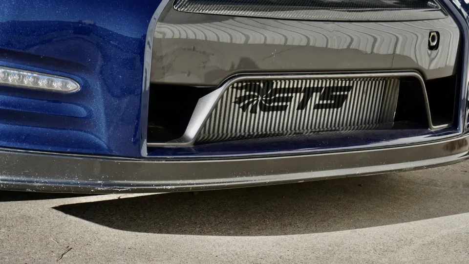 A close-up of a blue Nissan GT-R's front bumper, showcasing a Jotech intercooler and LED daytime running lights.