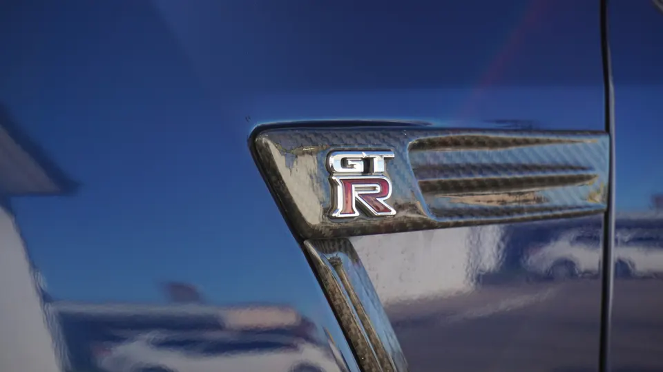 Close-up of a Nissan GT-R badge on a carbon fiber fender vent of a blue car