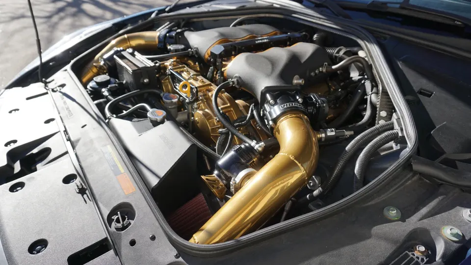 Close-up of a Nissan GT-R VR38DETT engine bay with custom gold turbo and induction piping, and an aftermarket air filter.