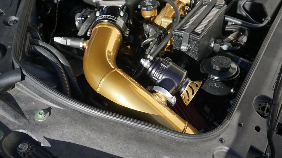 Detailed view of a custom gold intake pipe and blow-off valve in a high-performance car's engine bay.