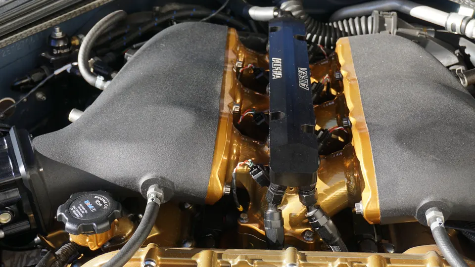 A close-up of a performance engine bay with an Alpha Performance fuel rail, custom intake manifold, and gold engine components.