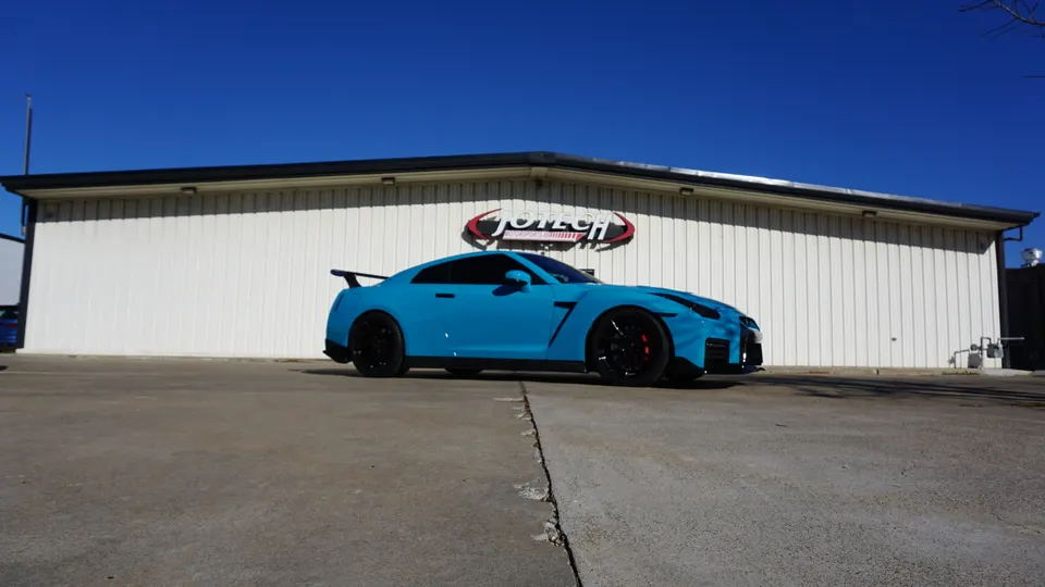 Blue Nissan GT-R parked outside Jotech Motorsports shop on a sunny day.