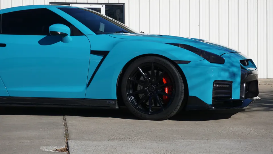 A blue Nissan GT-R with black wheels, red brake calipers, and carbon fiber aerodynamic parts parked outdoors.